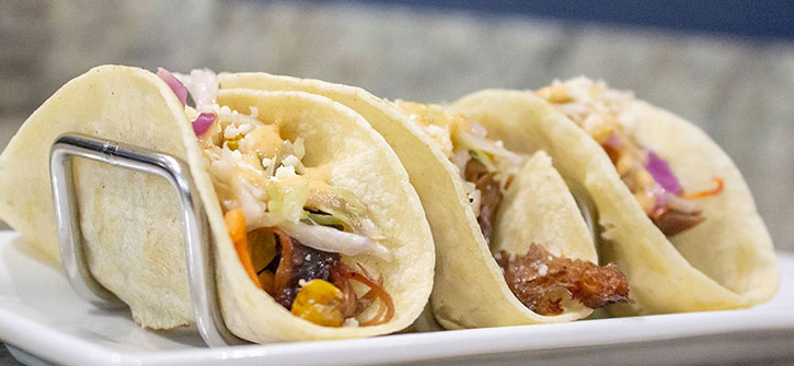 Three tacos on a plate with toppings