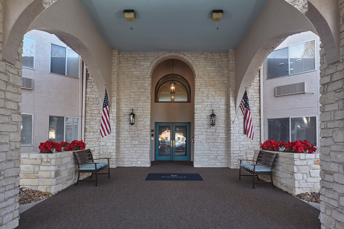 Entrance of Solstice Senior Living at Austin with potted plants and flags