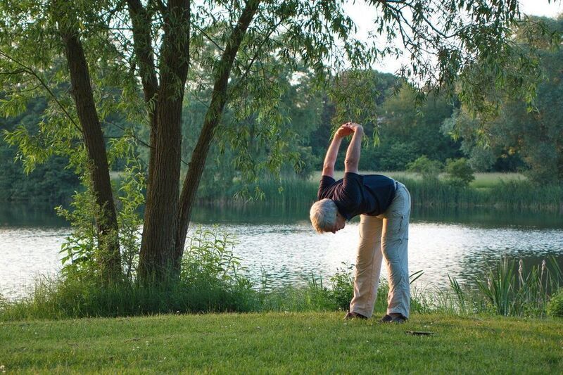 Senior stretching by a calm lake in a garden