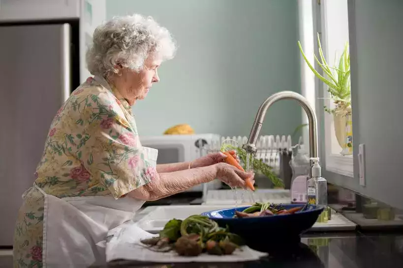 An elderly woman washing vegetables in a kitchen