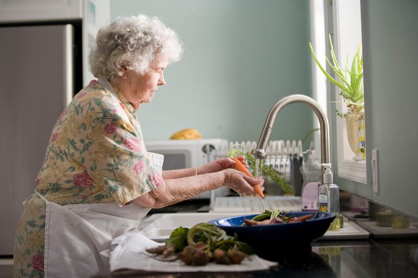 A senior woman washing vegetables in a kitchen