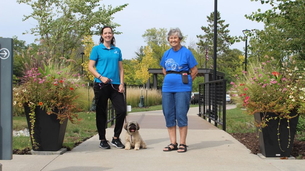 Resident and staff member walking a dog in a garden area