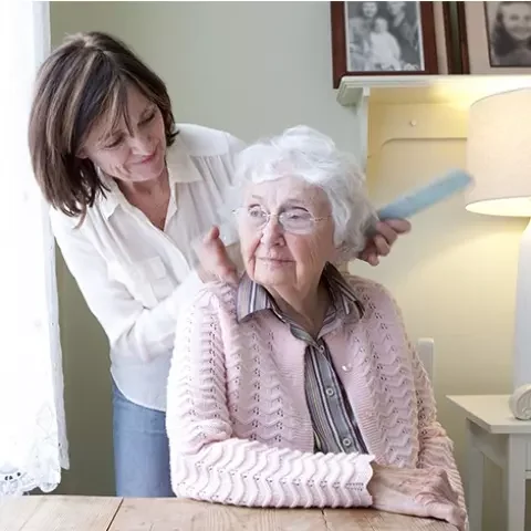 A staff member styling a resident's hair in a cozy room
