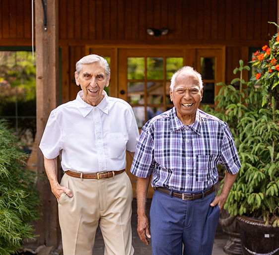 Two seniors smiling outside a facility entrance