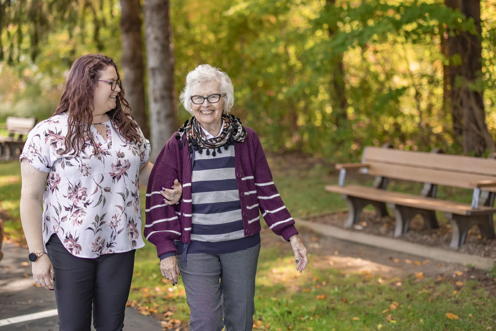 An elderly woman enjoying a walk with a staff member in a garden
