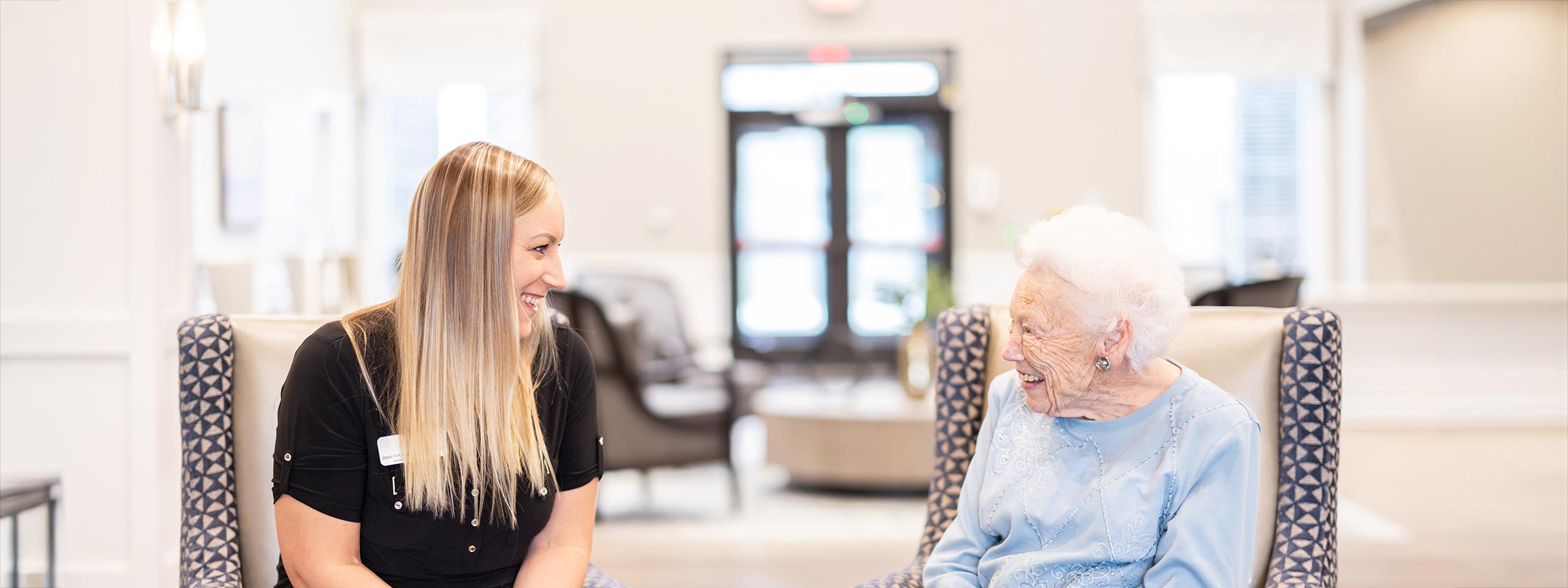 Caregiver laughing with a resident in a bright common area