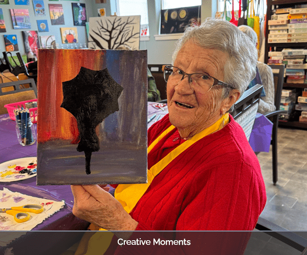 Elderly resident showcasing her painting in an activity room