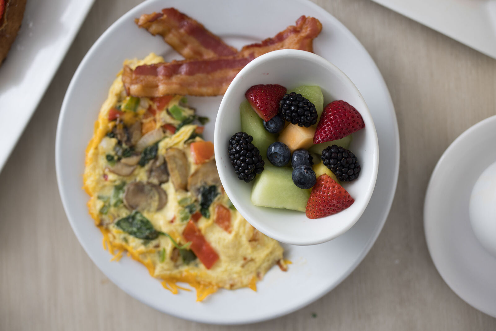 A plate of breakfast with an omelette, bacon, and fruit