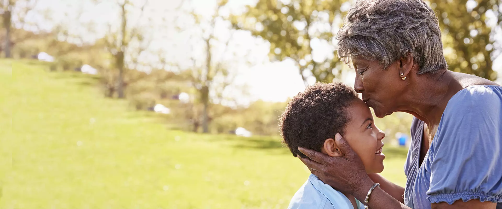 An elderly woman kissing a young boy in a green outdoor space.