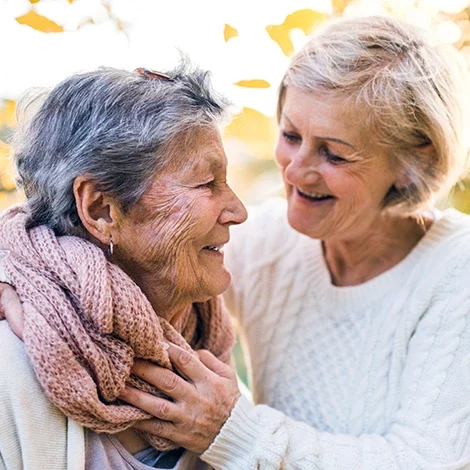 A smiling elderly woman with a caregiver outside