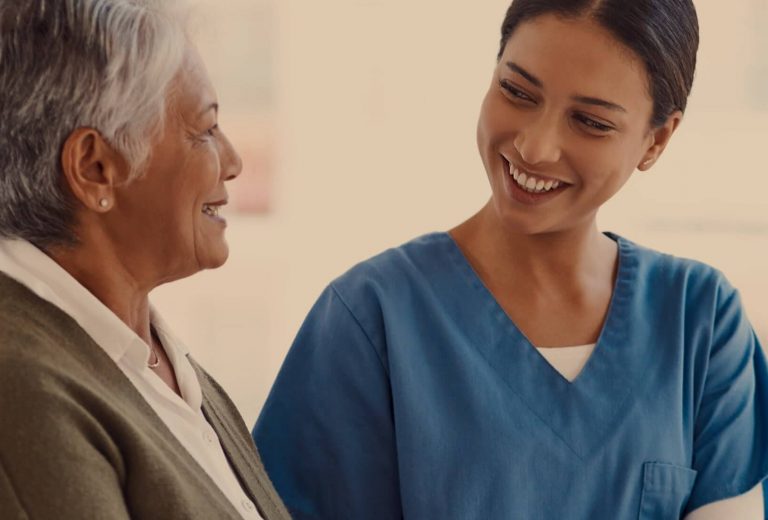 A nurse smiling with a senior resident in a bright setting
