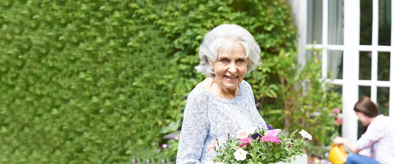 Elderly woman holding a pot of flowers in a garden