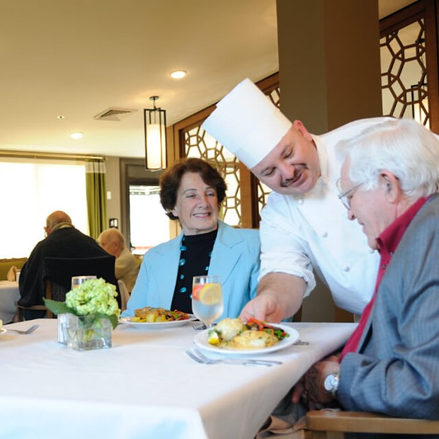 Chef serving food to residents in a dining area