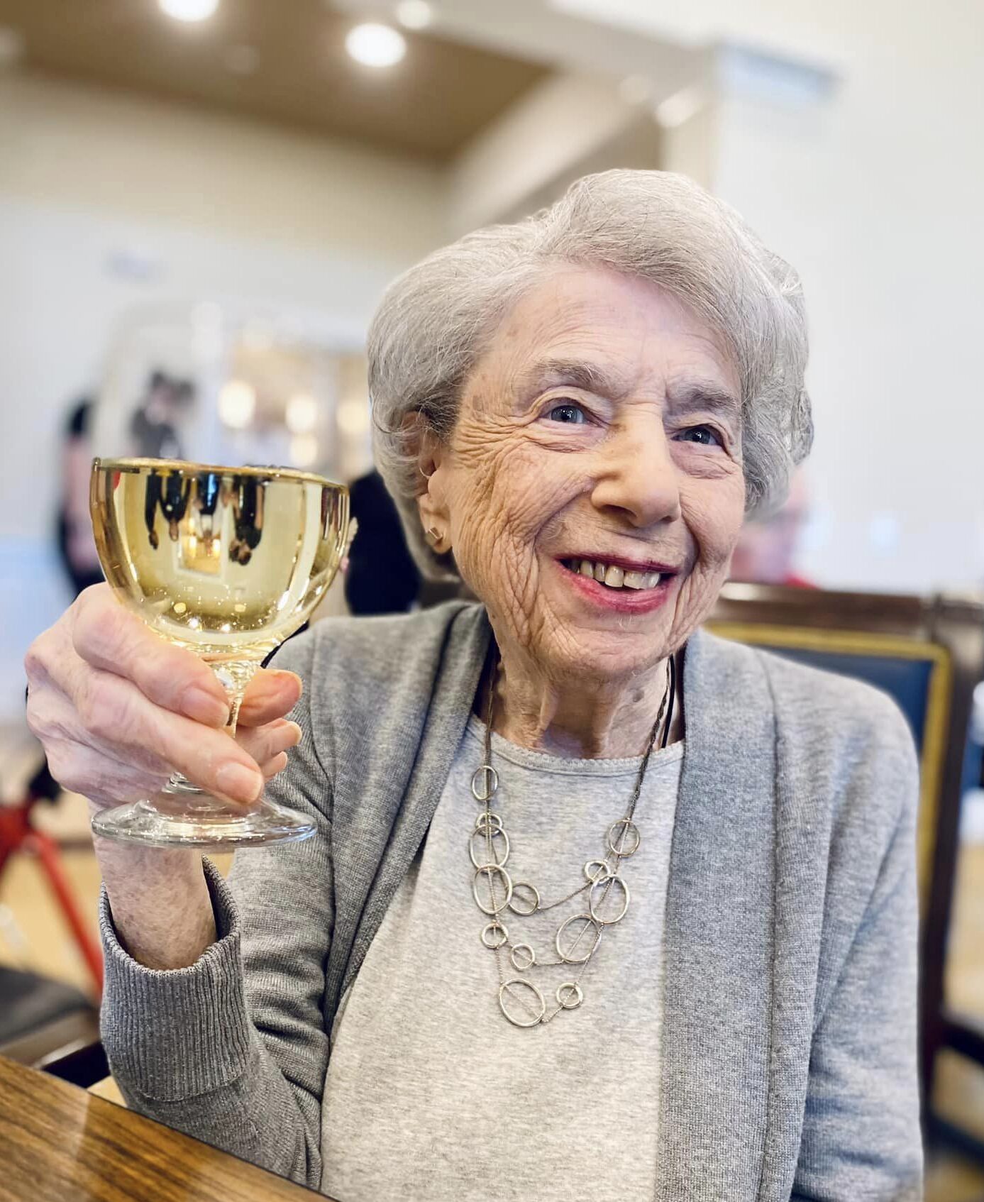 A smiling senior holding up a glass in a cheerful setting