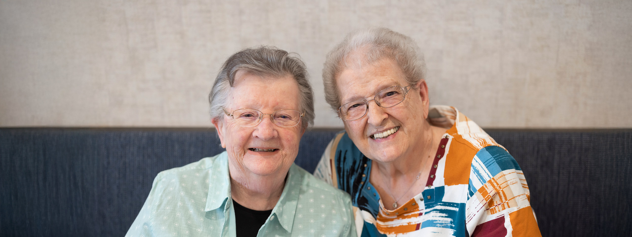 Two senior women smiling together in an indoor setting