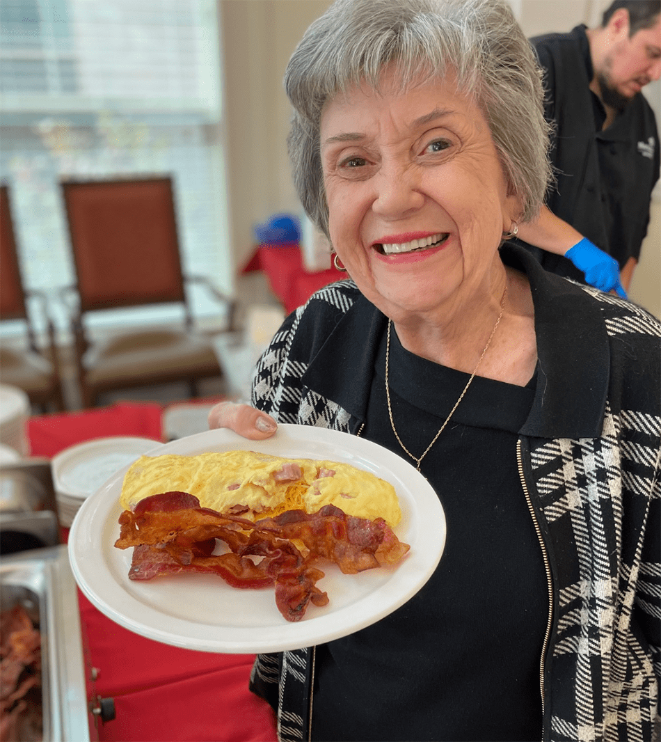 Resident smiling and holding a plate of bacon and omelet