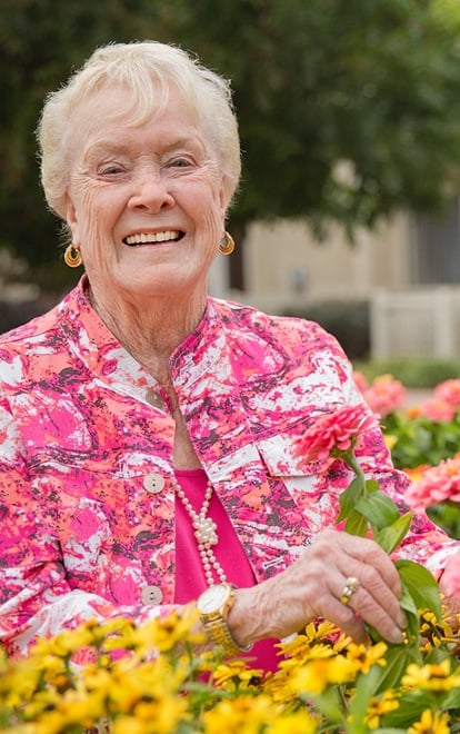 A smiling resident surrounded by colorful flowers