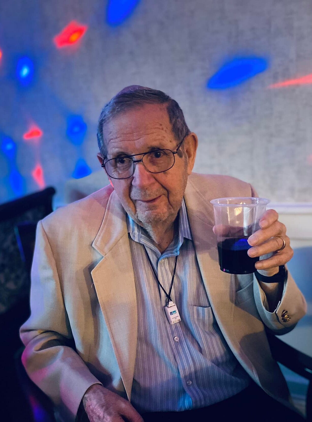An elderly man smiling while holding a drink