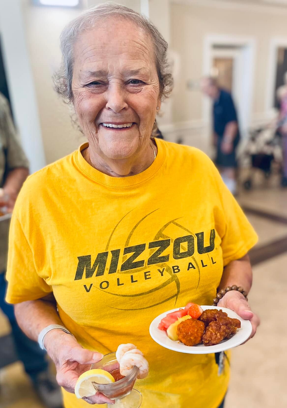 Resident smiling while holding a plate of food in the common area