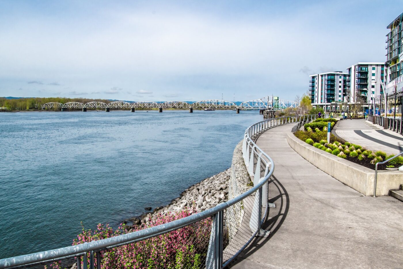 Pathway along a river with modern buildings in view