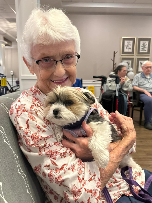 A smiling resident holding a small dog in a common area