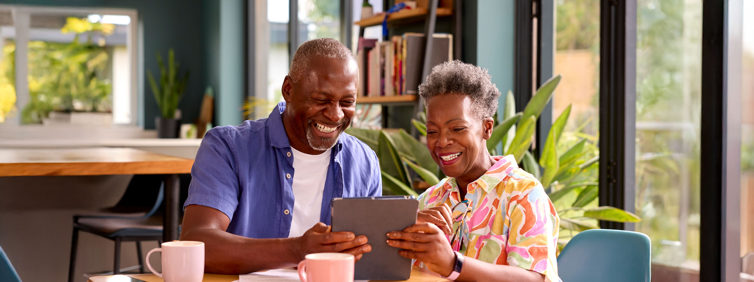 Two seniors joyfully using a tablet in a bright interior space