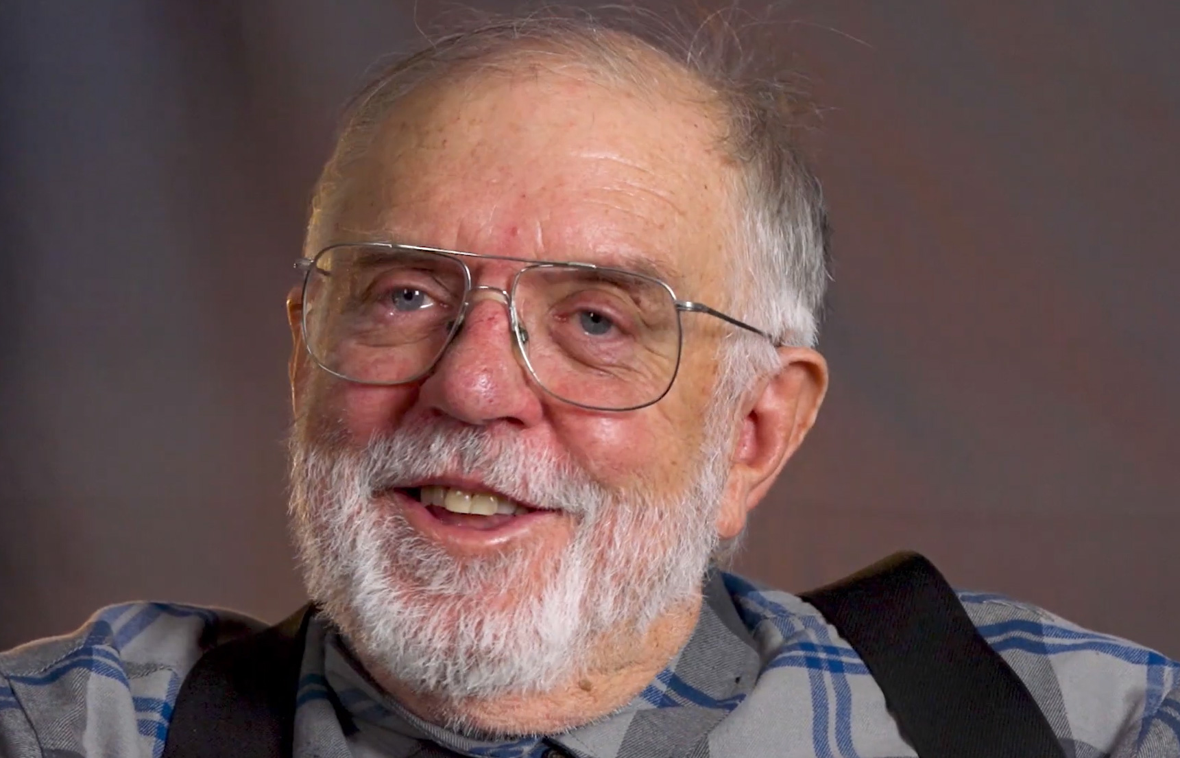 A smiling elderly man with glasses in a casual setting