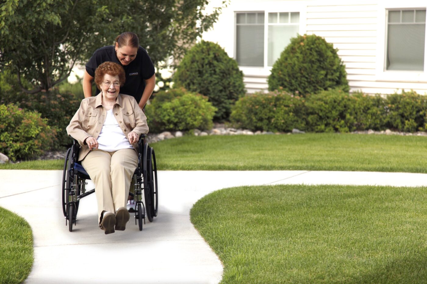 A resident being wheeled on a path by staff in a garden