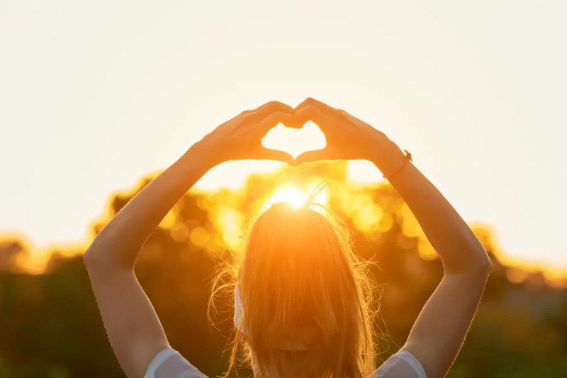 Person making a heart shape with hands at sunset