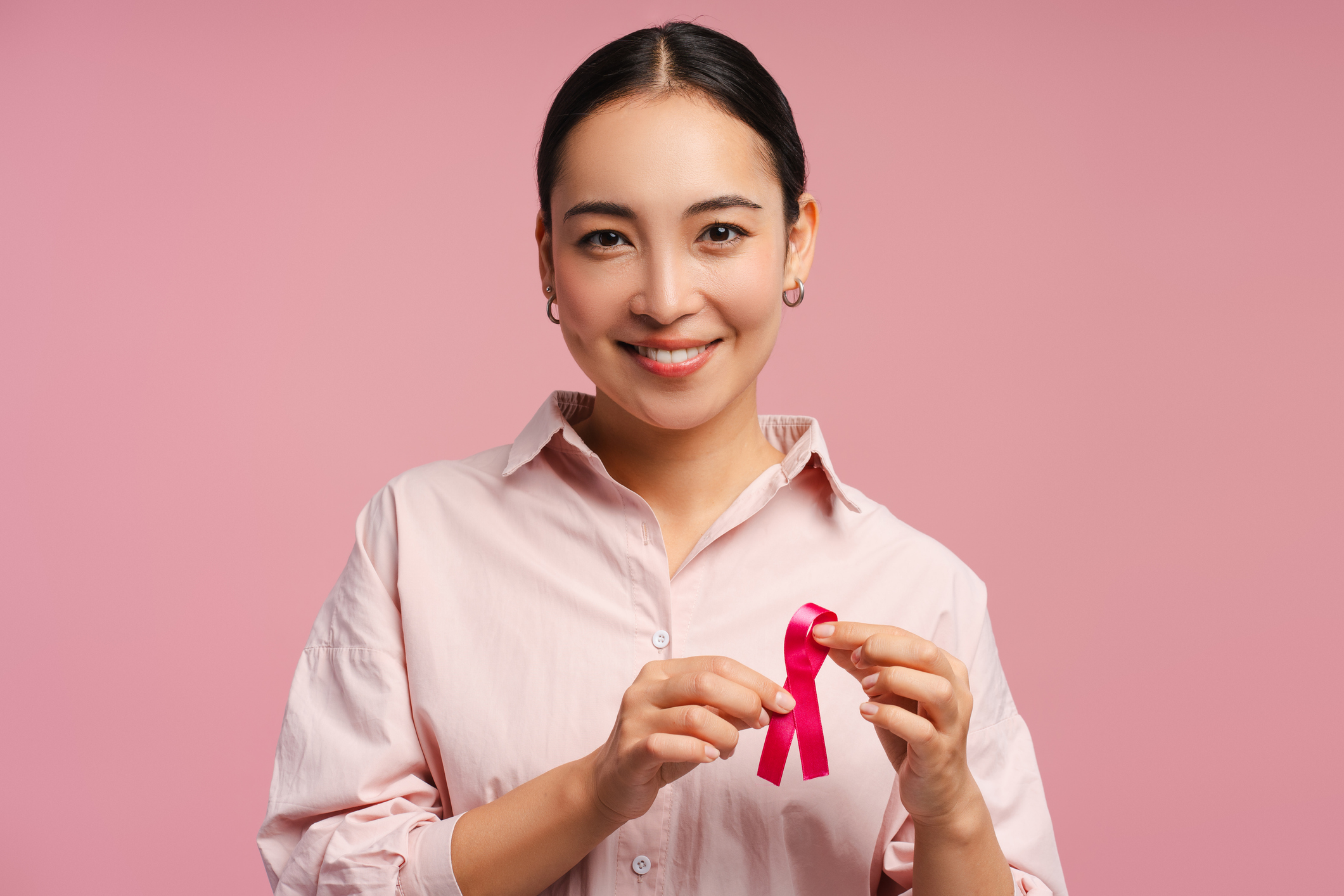 A woman holding a pink ribbon against a pink background