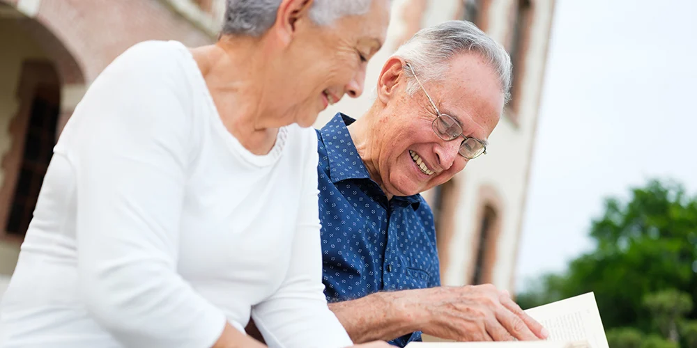 Two seniors enjoying a book outdoors