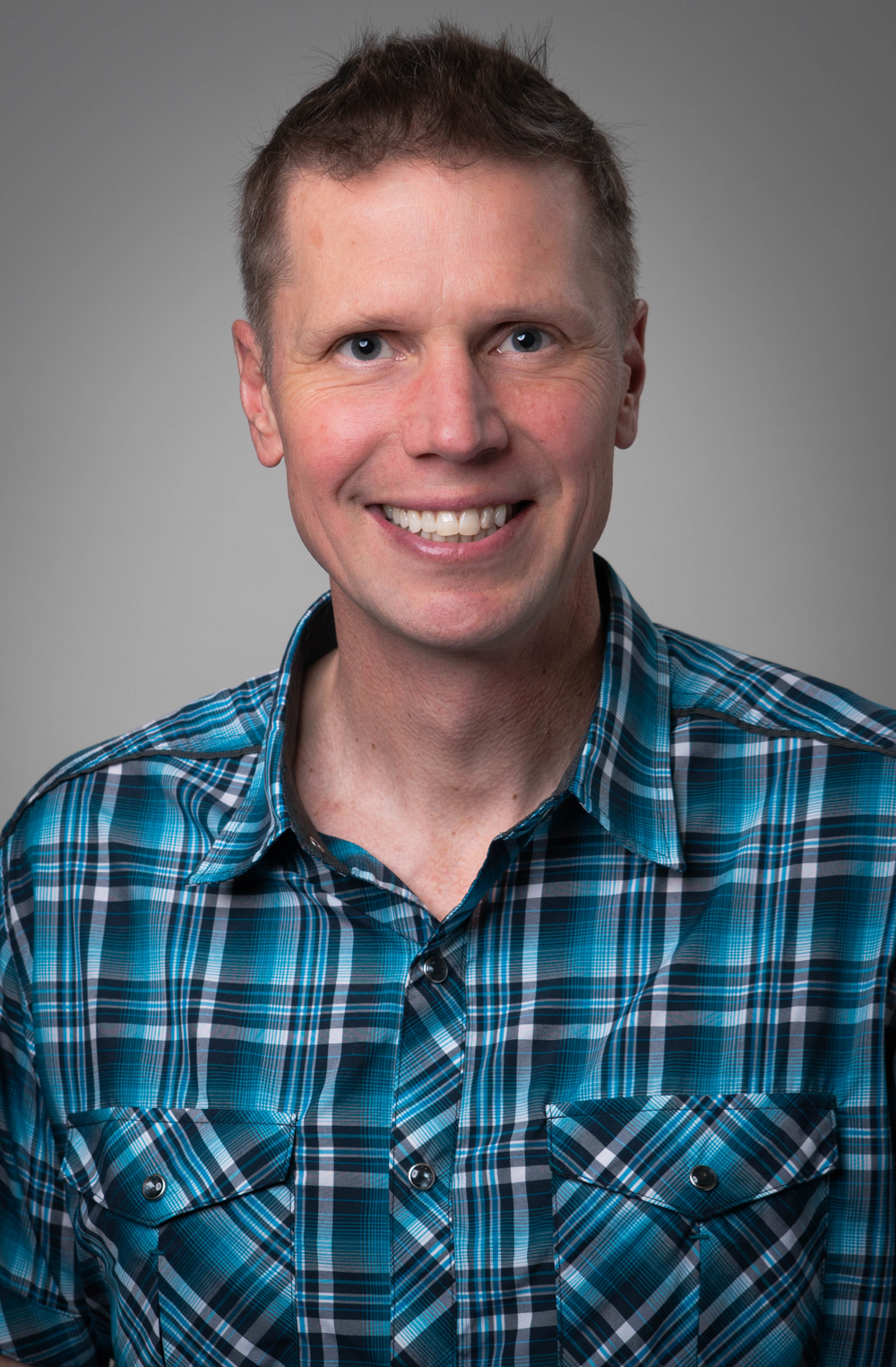 Smiling man in a plaid shirt against a neutral background