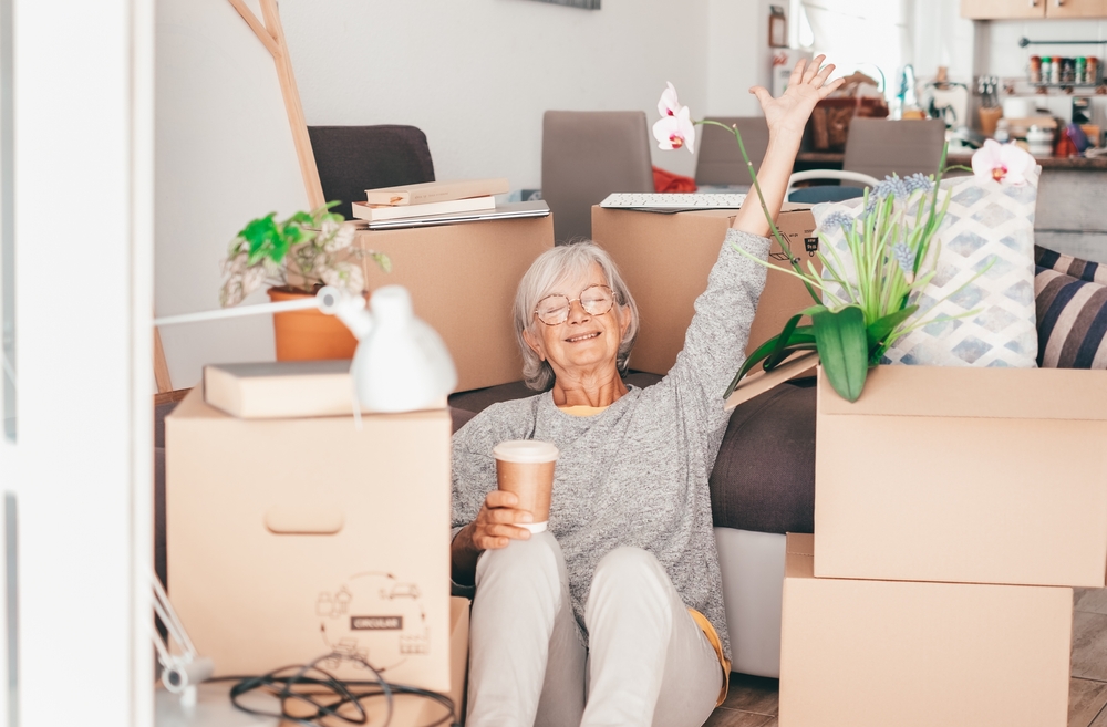 Senior woman surrounded by moving boxes, smiling and waving