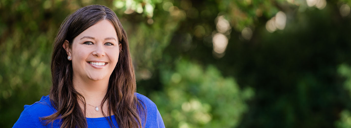 A staff member smiling outdoors in a green setting