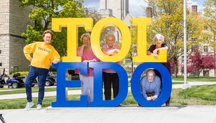 Residents celebrating outdoors near large letters spelling 'TOLEDO'