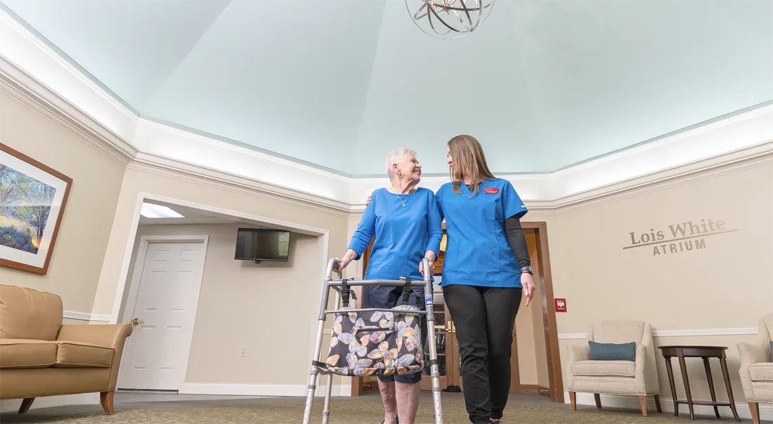 A caregiver assists a resident in an indoor atrium space