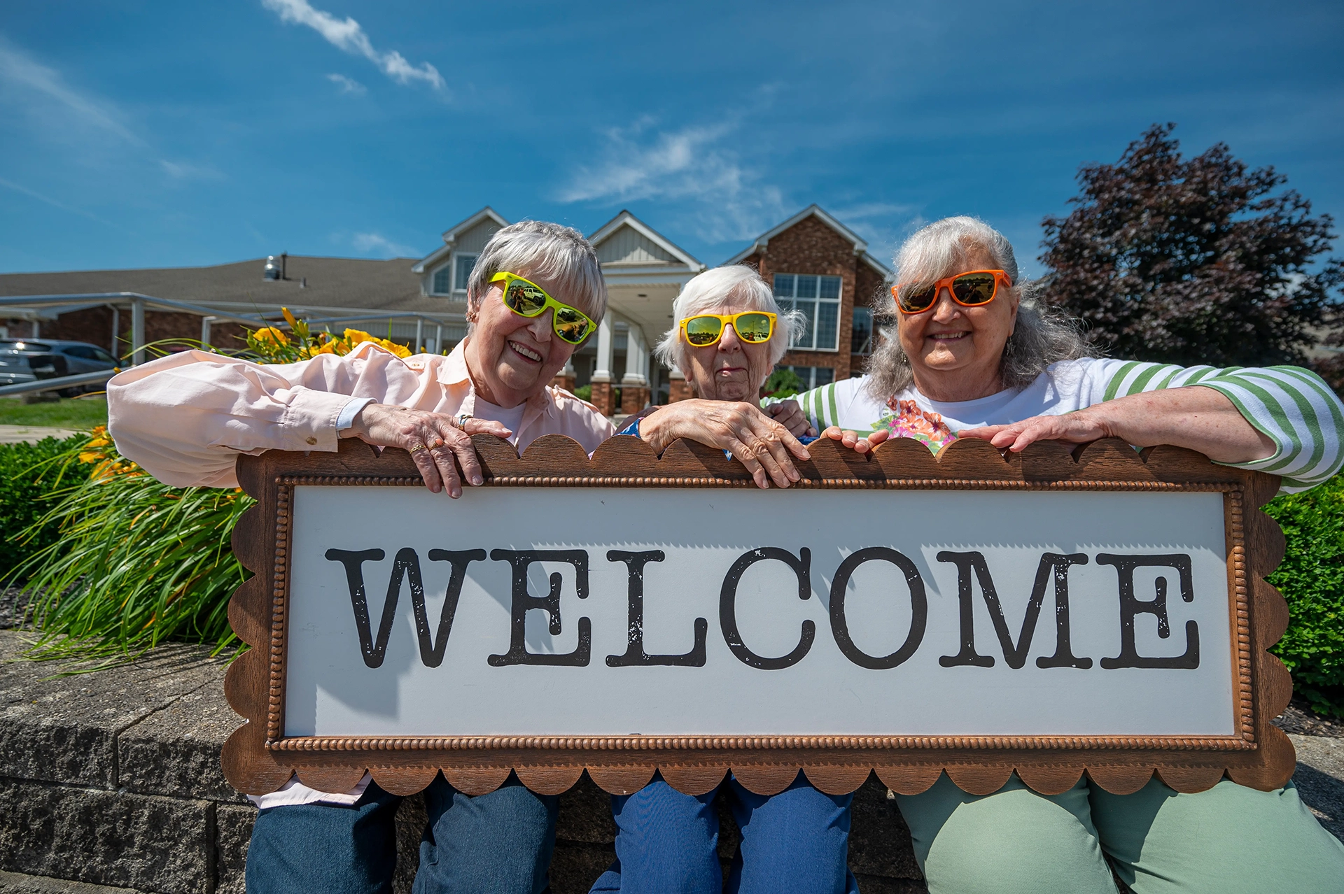 Three women holding a welcome sign outside the facility