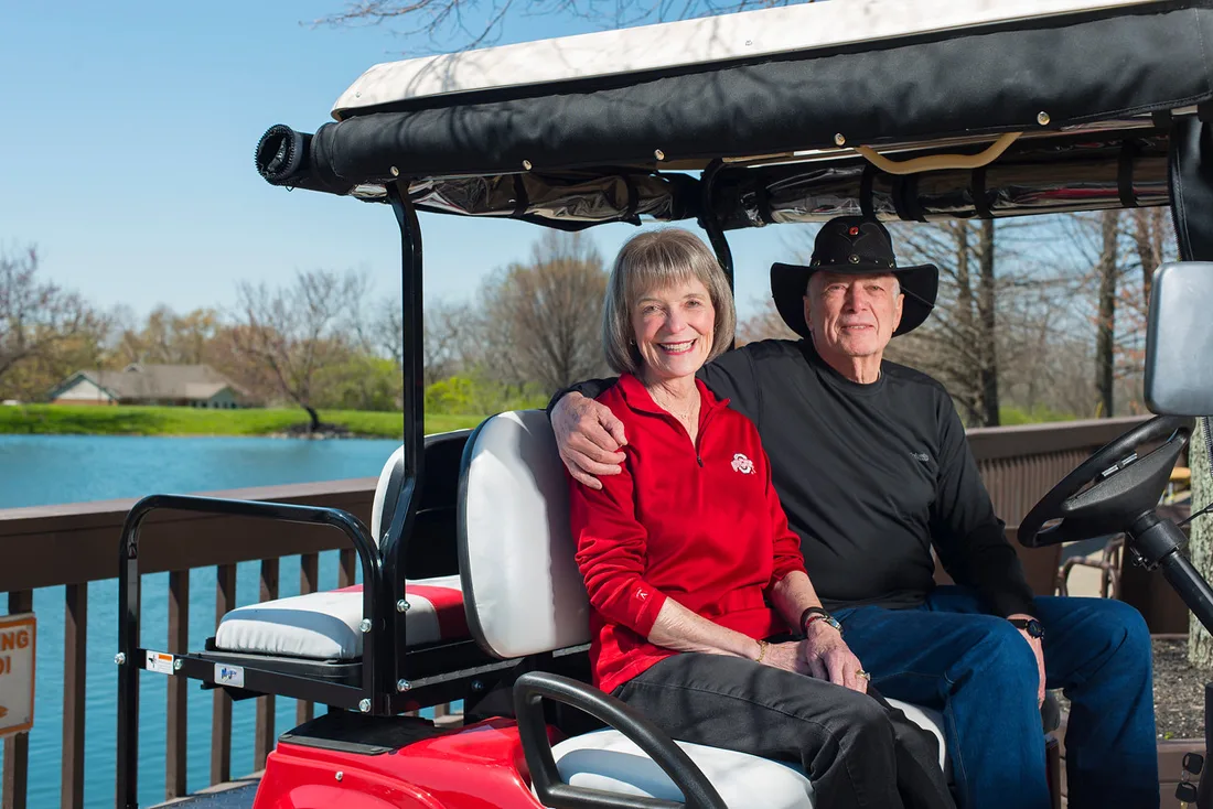 Older couple posing in a golf cart near a lake