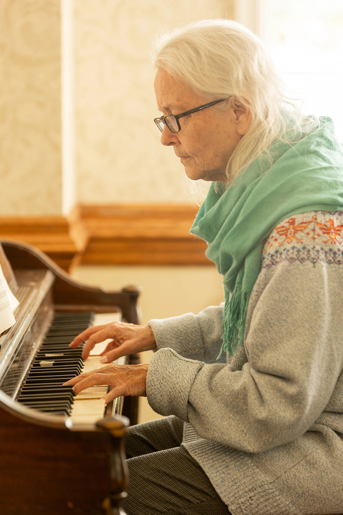 An elderly woman playing the piano in a cozy room