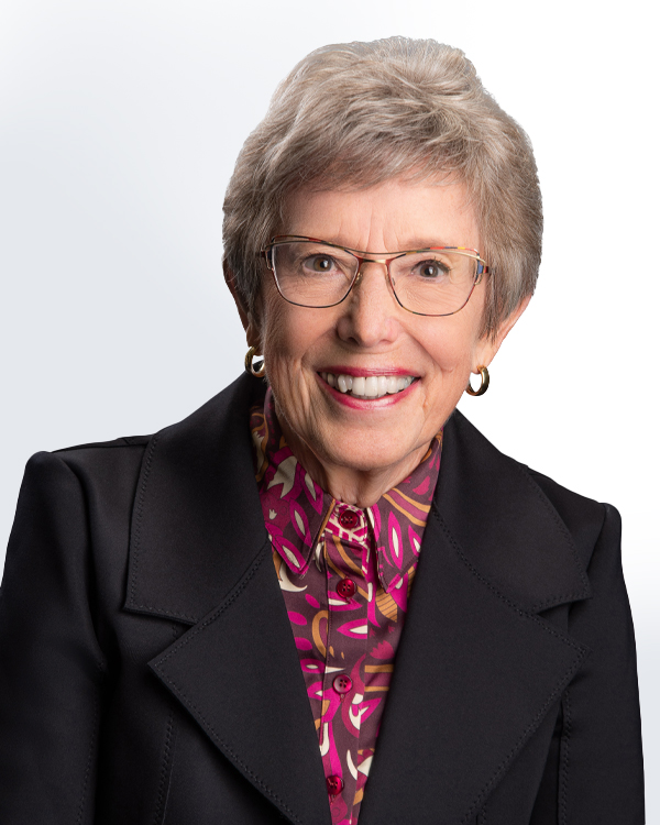 A smiling elderly woman with glasses, wearing a colorful blouse