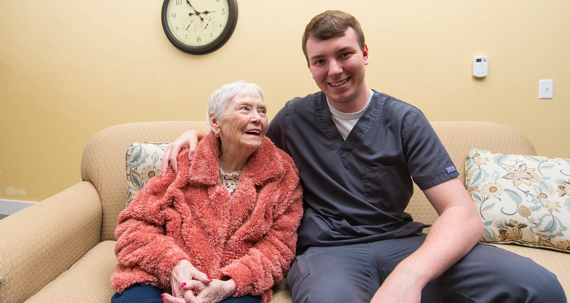 A caregiver and a resident smiling together on a couch