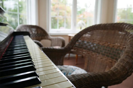 Close-up of a piano next to wicker chairs in a sunlit room