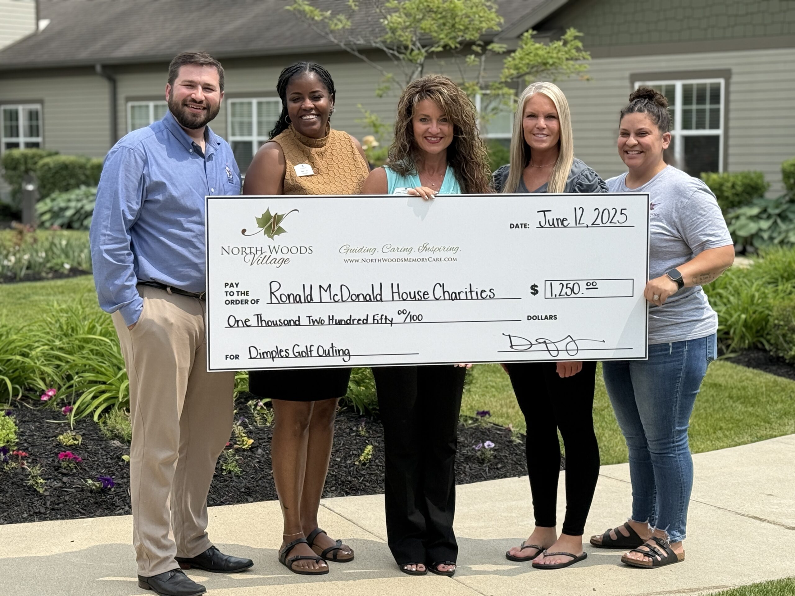 Staff presenting a large donation check outdoors.