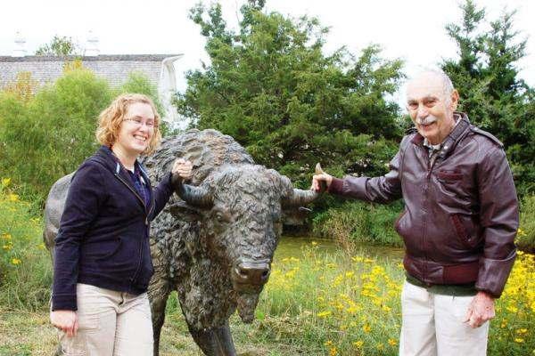Resident and staff member posing with a bison statue outdoors.