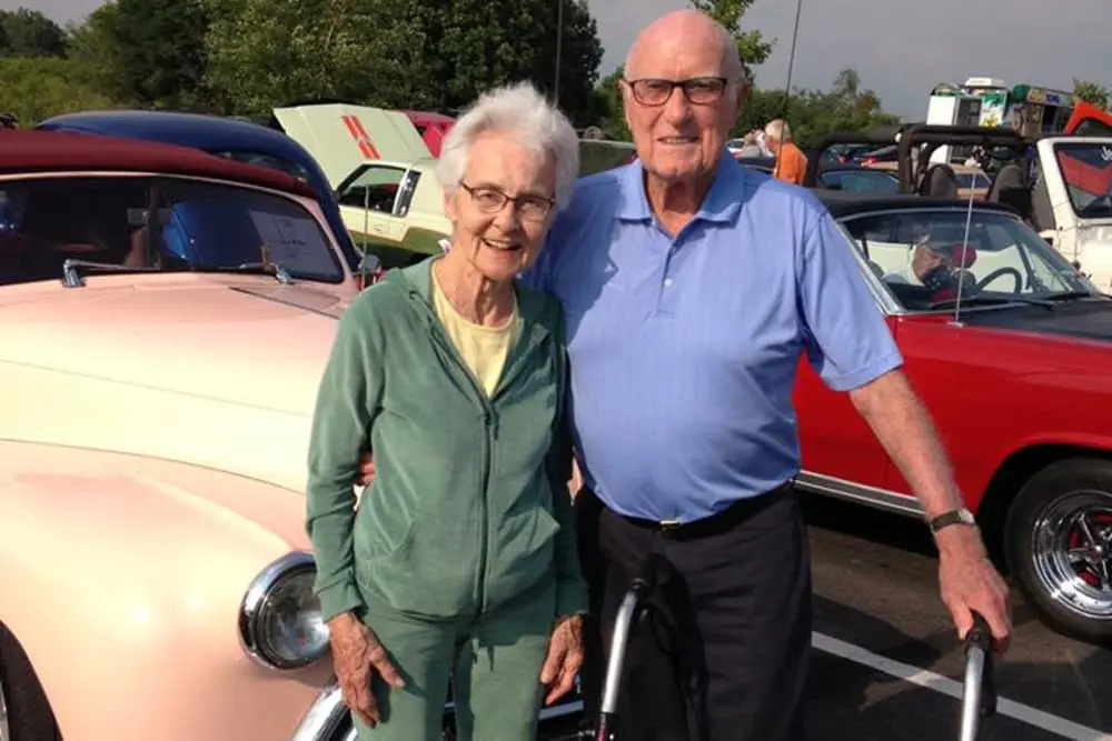 Elderly couple posing with a classic car outdoors.
