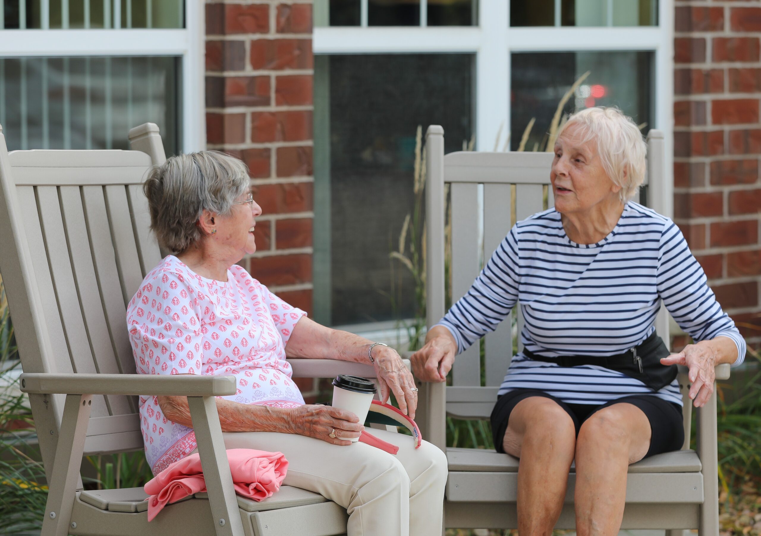 Two elderly women chatting on outdoor chairs.