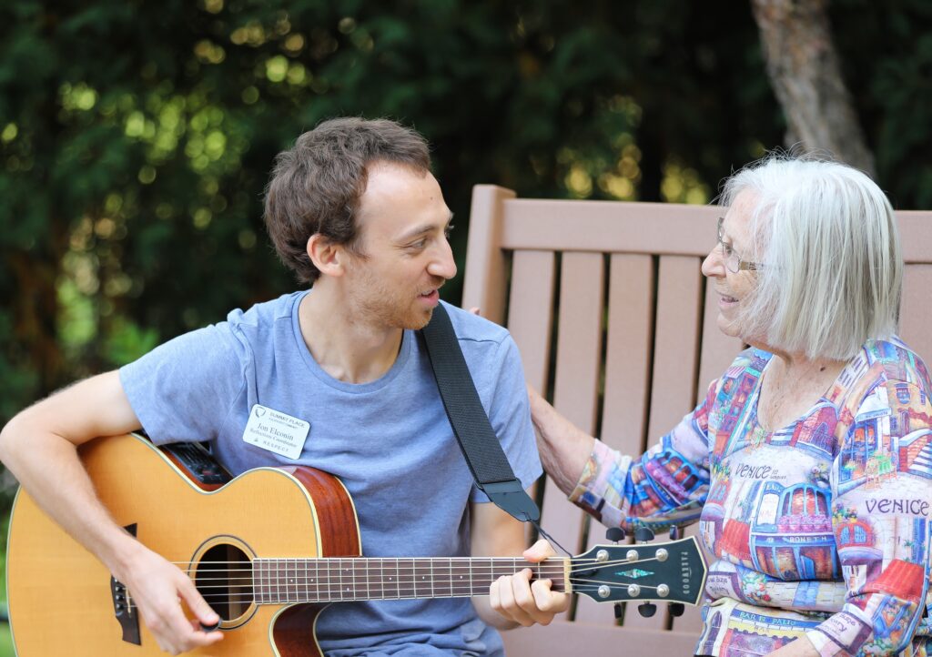 Staff member playing guitar with a resident in the garden.