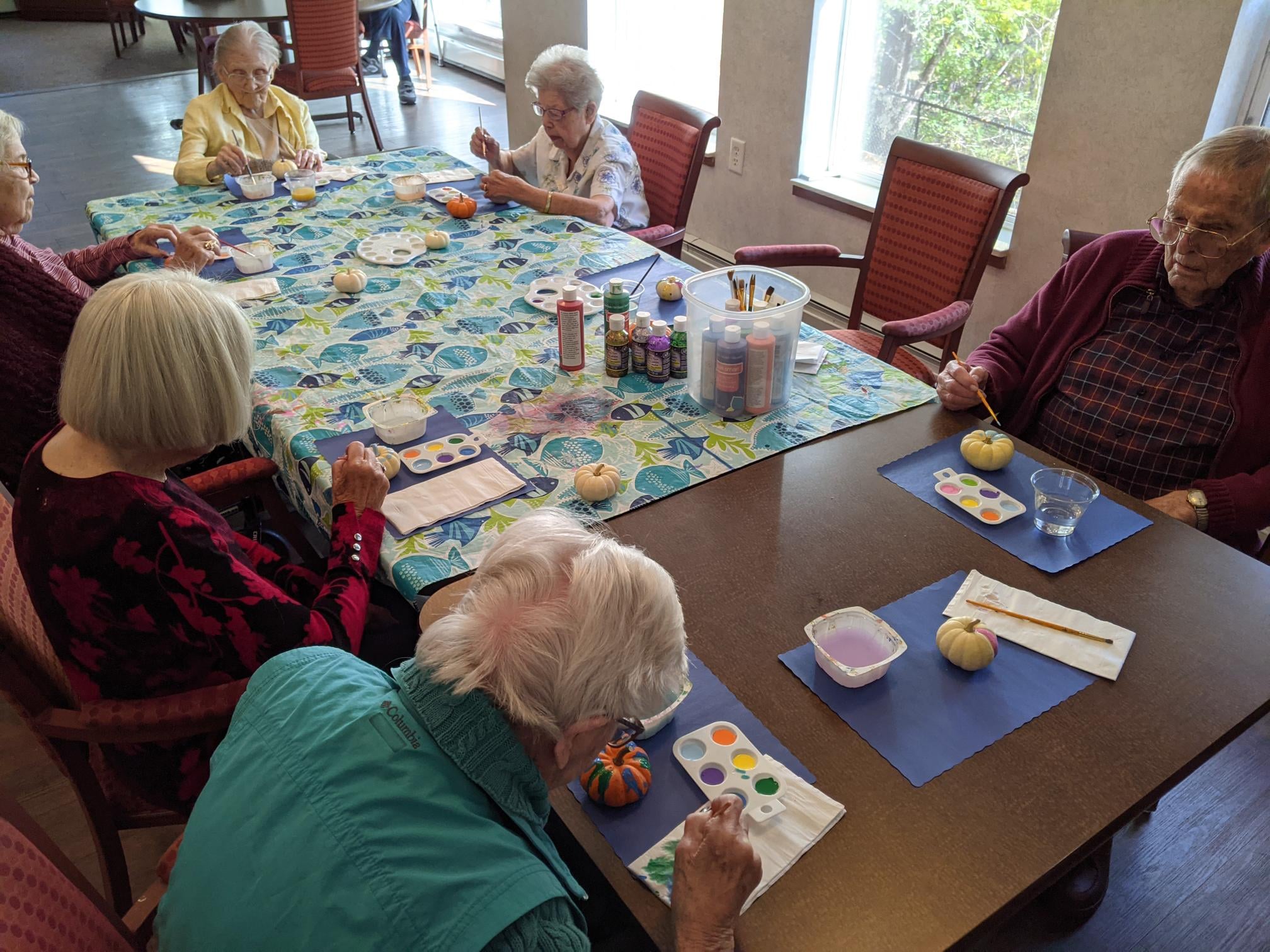 Seniors engaged in a painting activity at a communal table.
