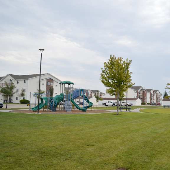 Playground area with green grass and buildings in the background.