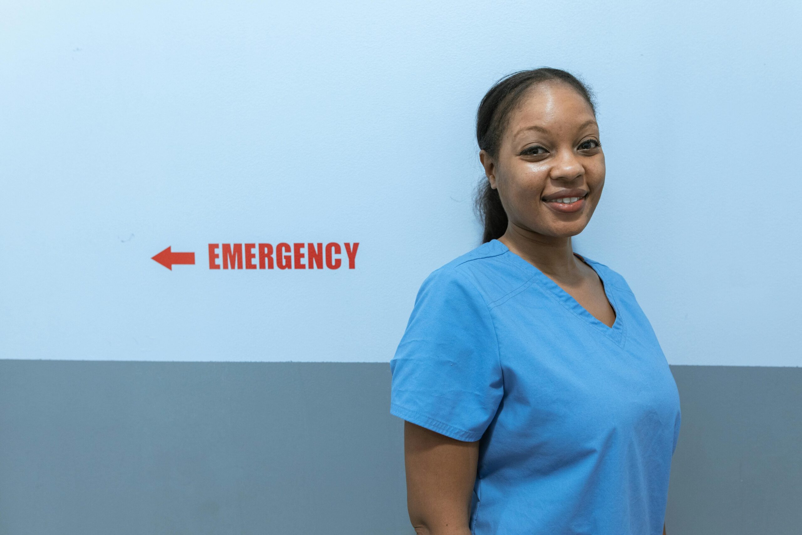 Healthcare worker in a hallway with emergency sign.